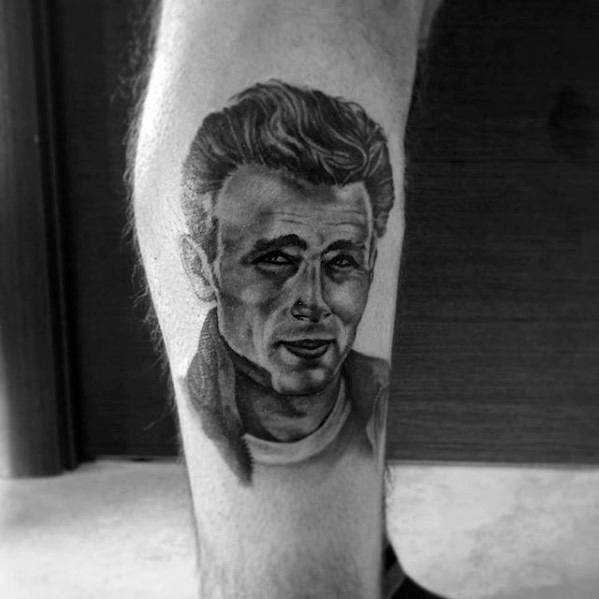 Black and grey calf tattoo of James Dean in a classic white tee and jacket, with a confident smirk and textured hair.