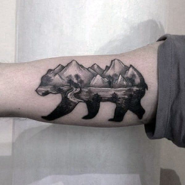 Bear silhouette tattoo filled with a detailed mountain, lake, and forest landscape, featuring a winding river across the body.