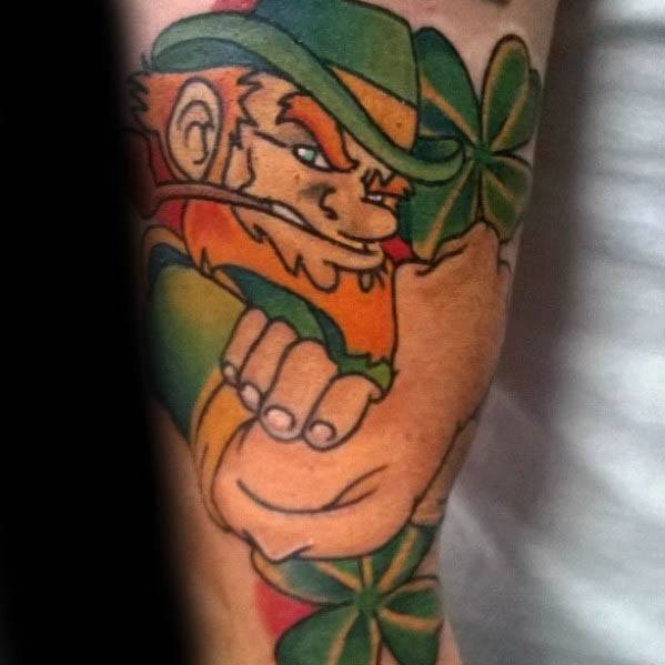 Bold leprechaun tattoo in a fighting pose with clenched fists, green hat, orange beard, and large shamrocks in the background.