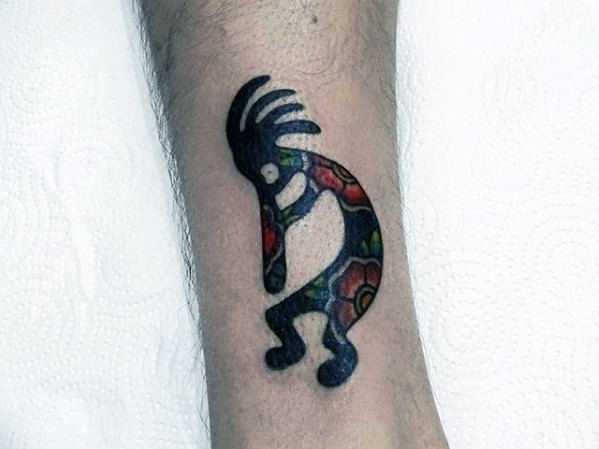 Kokopelli tattoo with bold black outlines and vibrant, multicolored tribal patterns, showcasing a lively design on the forearm.