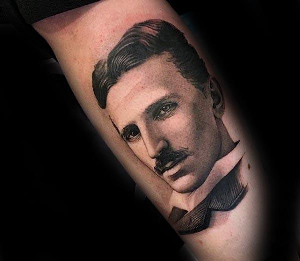Realistic black and grey portrait tattoo of Nikola Tesla with soft shading and a calm, introspective expression.