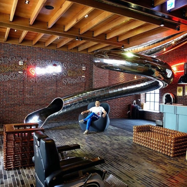 Modern lounge with a spiral slide, brick walls, and someone enjoying a chair