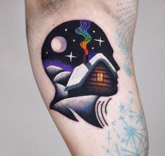 Tattoo of a head silhouette filled with a snowy cabin scene, colorful smoke, stars, and a glowing moonlit sky.
