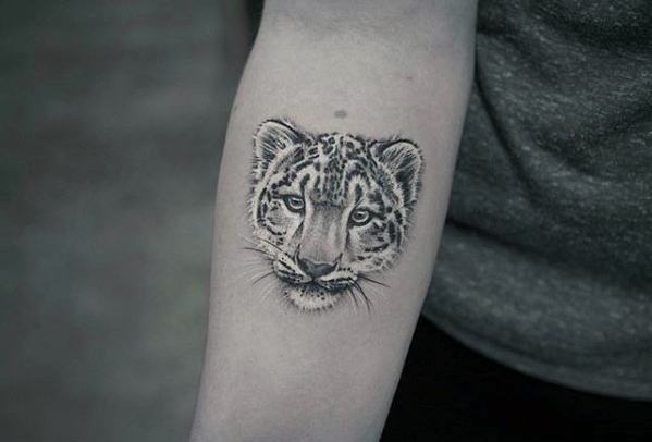 Minimalist snow leopard cub tattoo on the forearm, featuring fine black and gray linework with a calm and gentle expression.