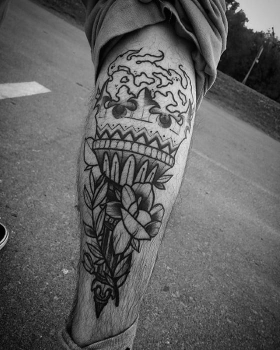 Black linework torch tattoo on the calf with swirling flames, a floral arrangement at the base, and bold ornamental detailing.