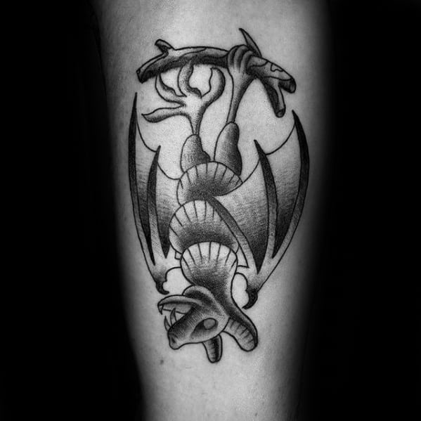 Black and grey traditional tattoo of a bat hanging upside down from a branch, with clean shading and smooth curves.