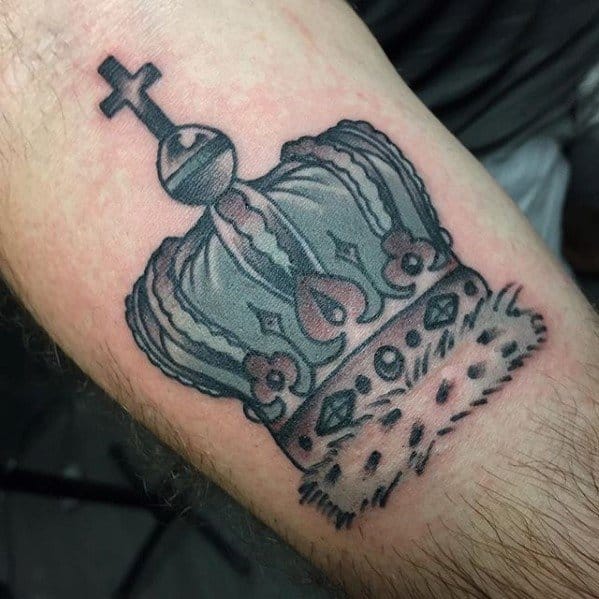 Black and grey crown tattoo with fur-trimmed base and jewel details, inked in a bold, traditional style on the upper arm.