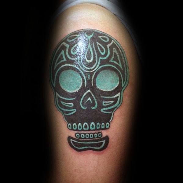 Colorful tribal sugar skull tattoo on upper arm with bold black outlines and teal accents, featuring simple yet striking shapes.