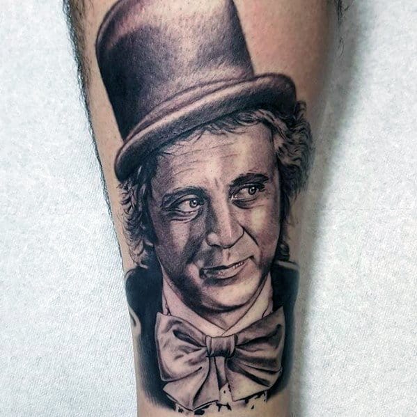 Black and grey Willy Wonka tattoo showing a soft smile, detailed curls, classic top hat, and a large bow tie with realistic shading.