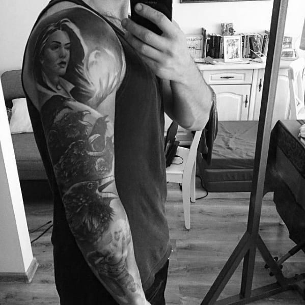 Black and grey Witcher sleeve tattoo featuring Yennefer casting a spell, with detailed ravens and floral elements flowing down the arm.