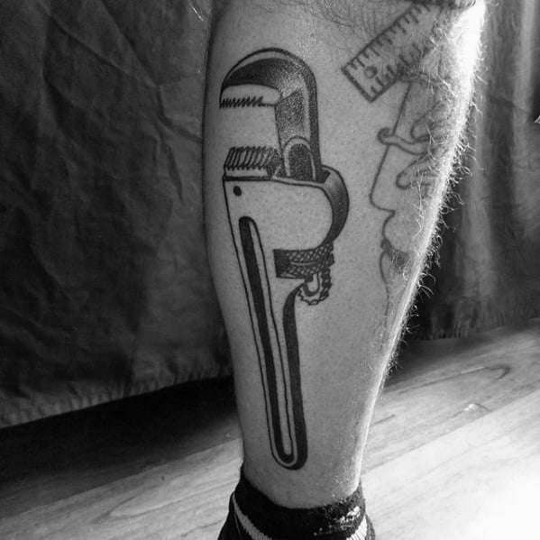 Blackwork tattoo of a detailed pipe wrench on the calf, featuring clean lines and subtle shading for a bold, classic look.