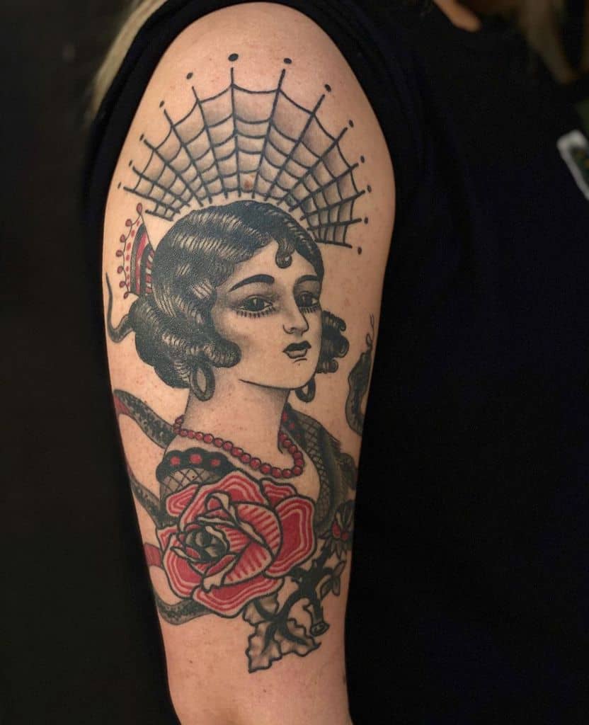 Traditional tattoo of a gypsy woman with a spiderweb halo, red roses, and bold black shading on the upper arm.