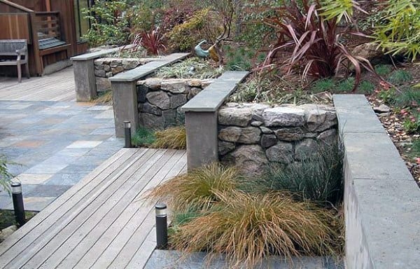 Stone and concrete retaining walls with integrated planters, surrounded by a wooden deck and modern lighting.