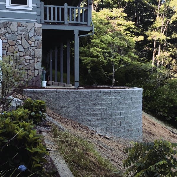 Curved concrete retaining wall supporting a raised patio with a forested hillside backdrop.