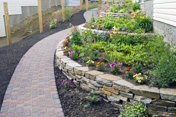 Stone retaining wall with colorful flower beds alongside a curved brick walkway.