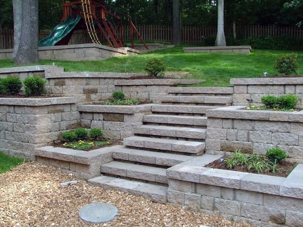 Tiered retaining walls with built-in steps, small shrubs, and a playground in the background.