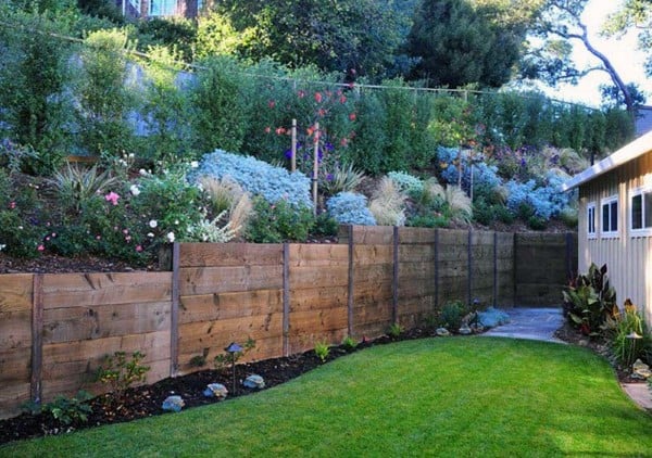 Wooden retaining wall with vibrant layered garden beds and a neatly manicured lawn.