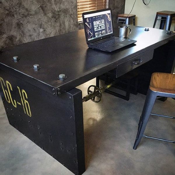 Industrial-style desk with a laptop and mug on top, featuring metal fixtures and a decorative wheel handle