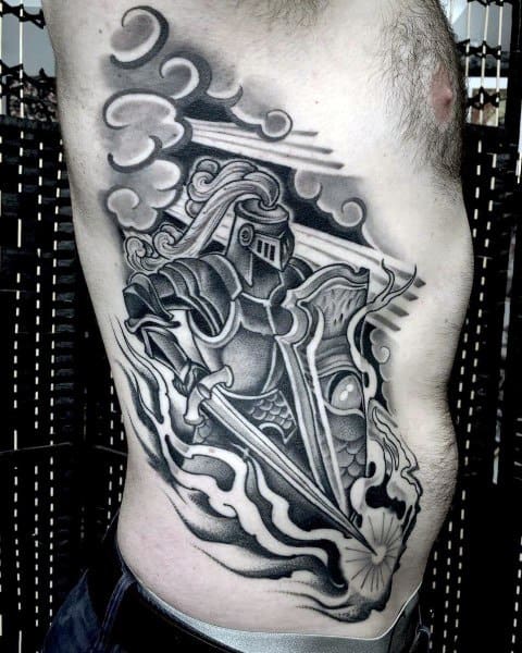 Striking side torso tattoo of a stylized knight in armor holding a sword and shield, surrounded by dramatic clouds and bold black shading.