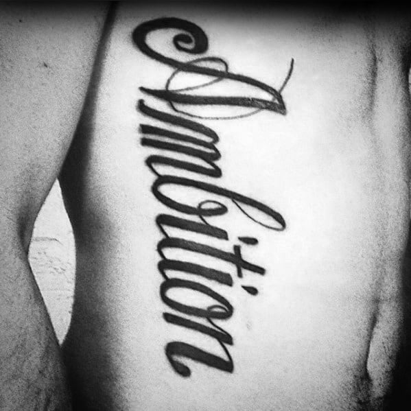Tattooed "Ambition" in elegant cursive on a person's ribcage, showcased beautifully in black ink