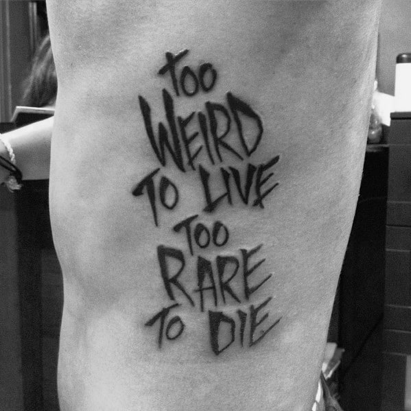 Bold black ink tattoo featuring the famous Hunter S. Thompson quote "Too Weird to Live, Too Rare to Die" in a sharp, graffiti-style font.