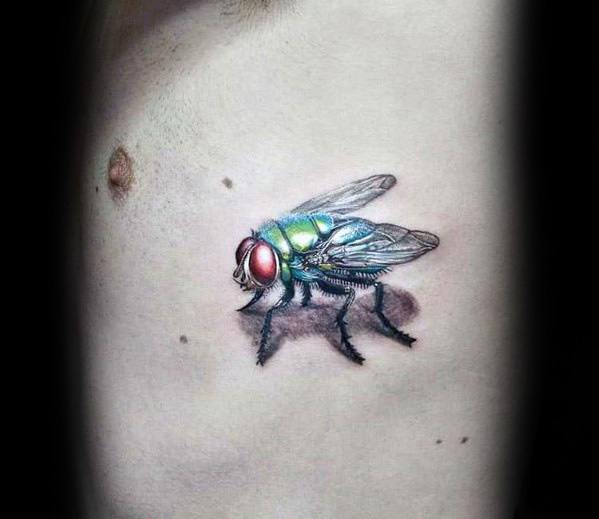Hyper-realistic fly tattoo on the chest with metallic green and blue tones, vivid red eyes, and a cast shadow for a 3D illusion.