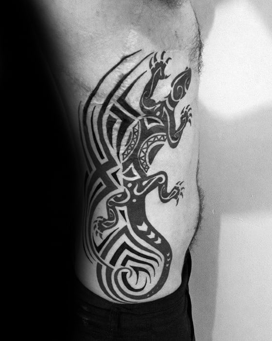 Large tribal gecko tattoo on the side of the torso with bold black lines, geometric patterns, and a dynamic, spiraled tail design.