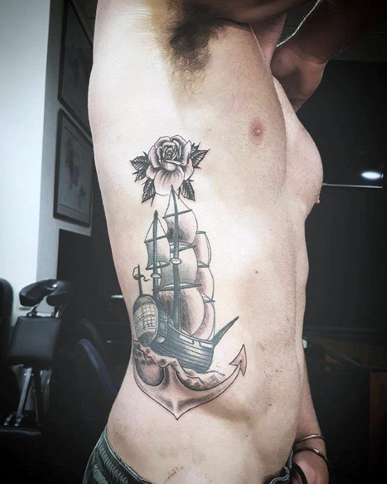 Man with tattoo of a sailing ship, anchor, and rose on left side ribcage
