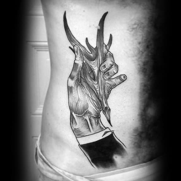 A black and white tattoo resembling a hand clutching sharp, organic-looking shapes is sketched with pencil-like precision on a person's side