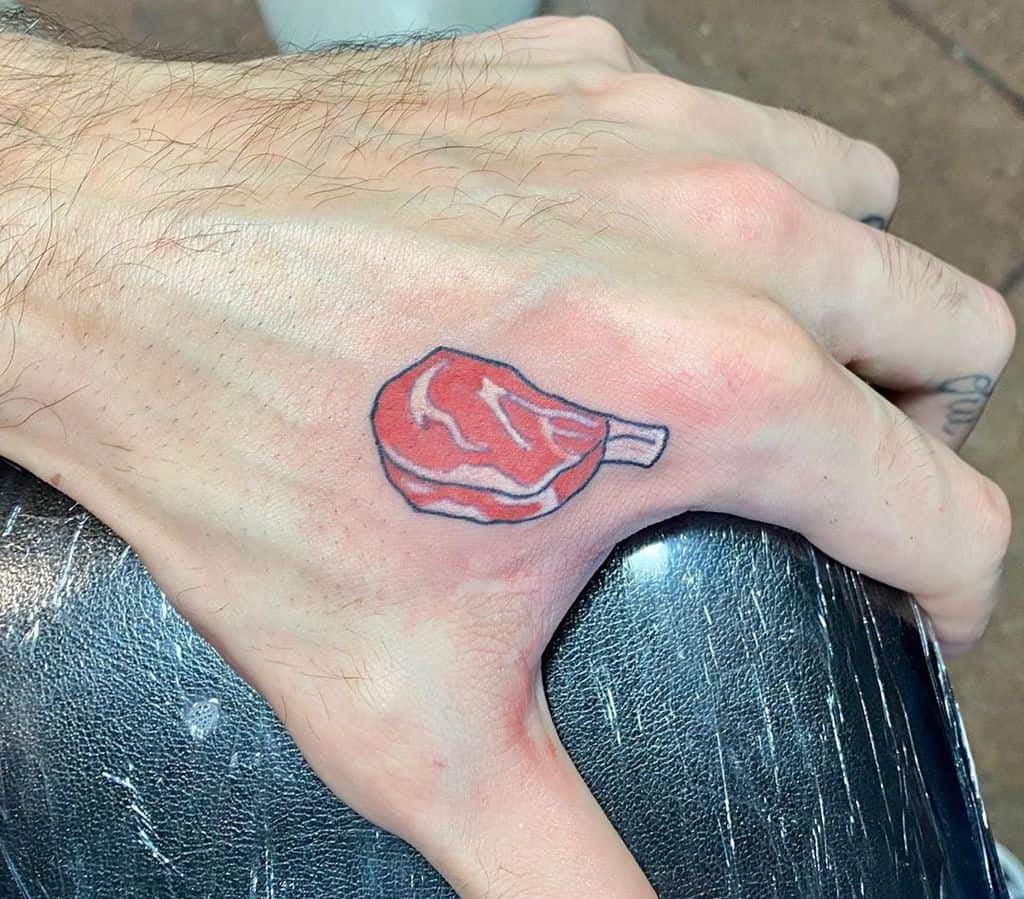 A small colorful tattoo of a cartoon-style steak placed on the hand, creating a fun and quirky design.