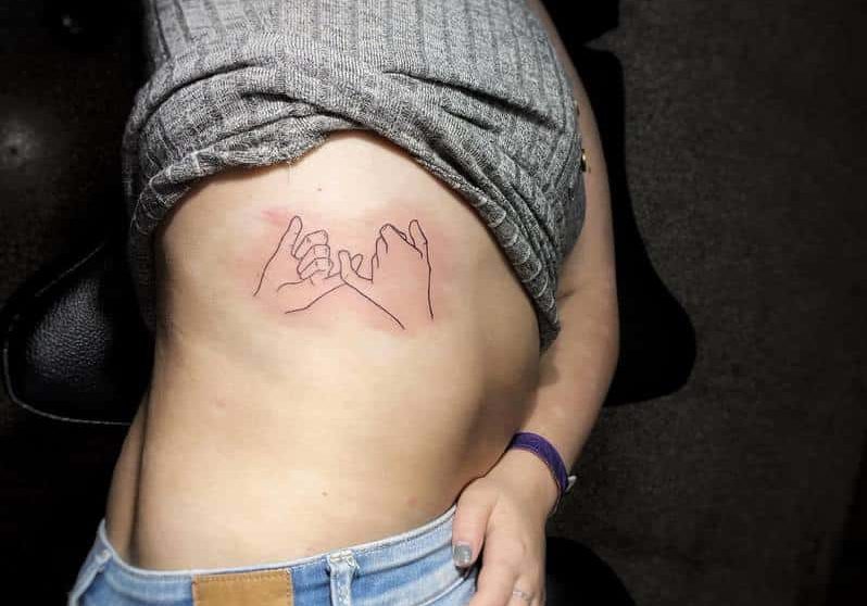Woman lying down with a tattoo of two hands linked at the pinkies