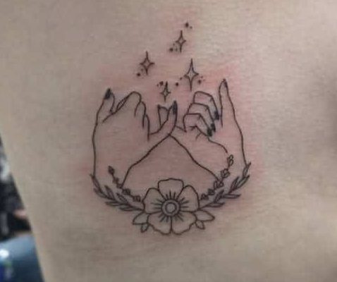Tattoo of two hands doing a pinky promise with stars above and a flower with leaves below