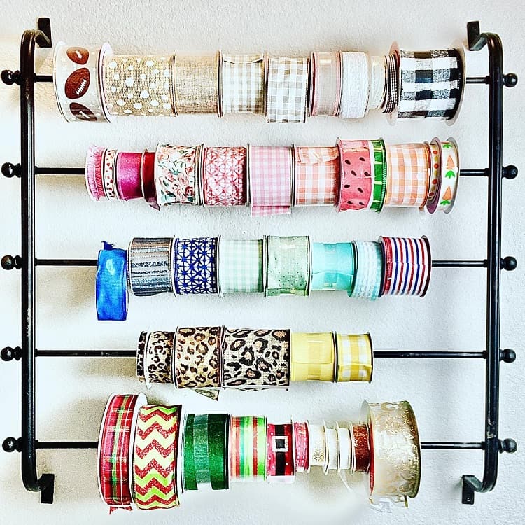 A wall-mounted rack displaying multiple colorful ribbons on spools, organized by patterns and styles