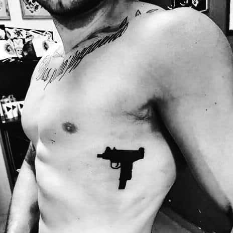 Small black Uzi silhouette tattoo on the ribcage, featuring a minimalist design with bold contrast against the skin.