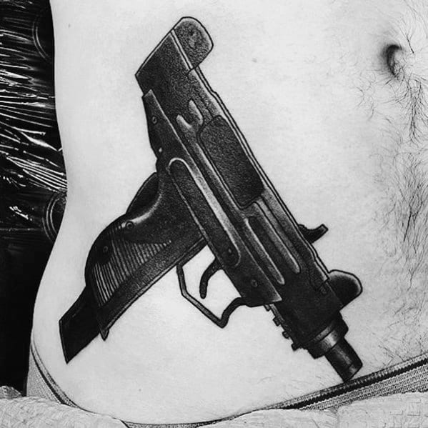 Realistic black and grey Uzi tattoo on the lower abdomen with bold shading and fine details, creating a striking and lifelike firearm design.