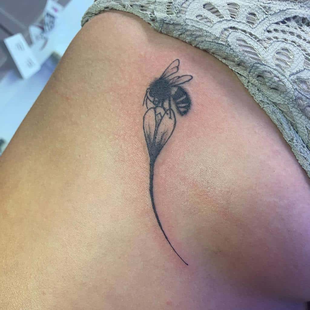 Minimalist black ink tattoo of a bee resting on a delicate violet flower, symbolizing nature, pollination, and harmony