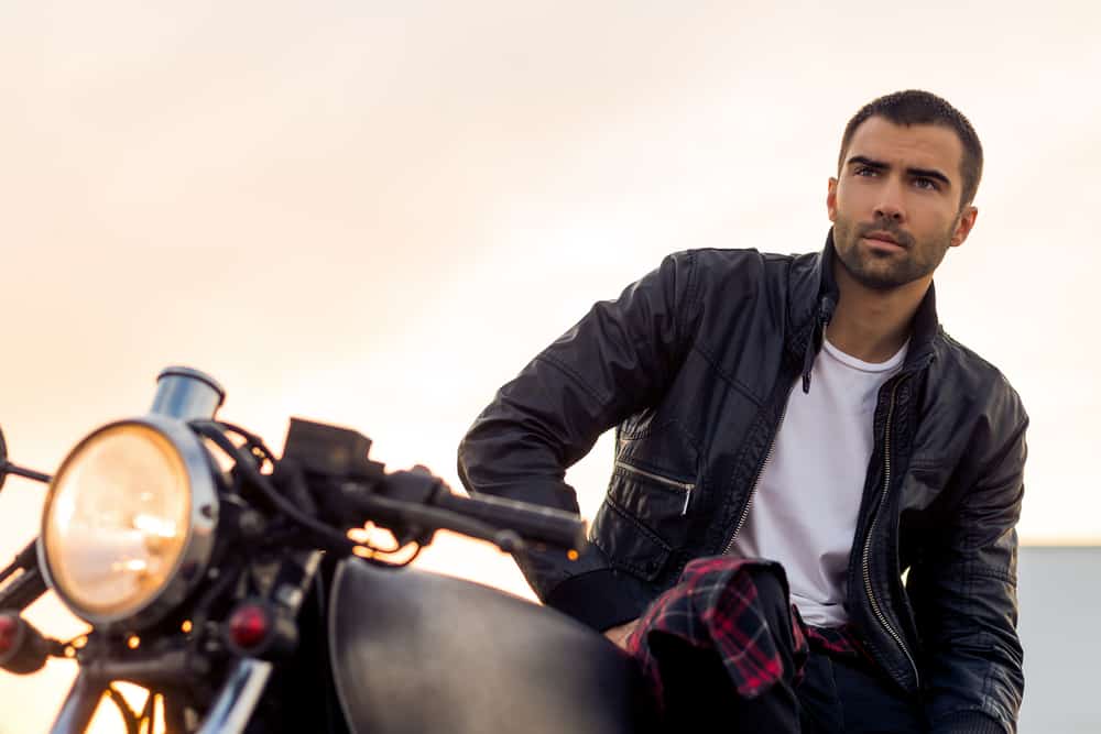 A man wearing a leather jacket and white t-shirt and sitting on a motorcycle
