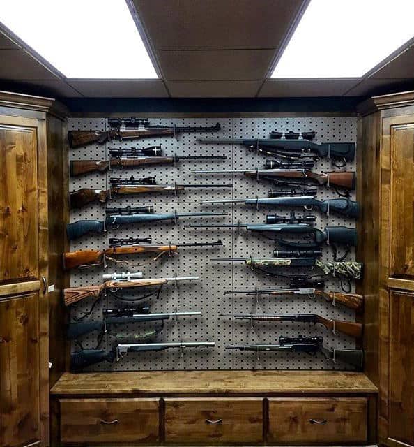 Gun room with pegboard wall displaying rifles and wooden cabinets with storage drawers.