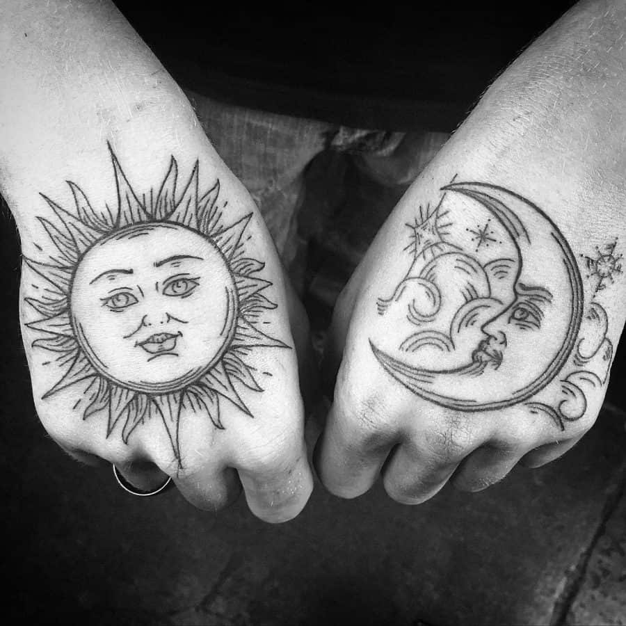 Black ink hand tattoos featuring a radiant sun with a serene face on one hand and a crescent moon with clouds and stars on the other.