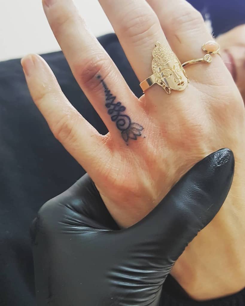 Unalome tattoo with a lotus on the finger, symbolizing spiritual growth, resilience, and the journey toward enlightenment.