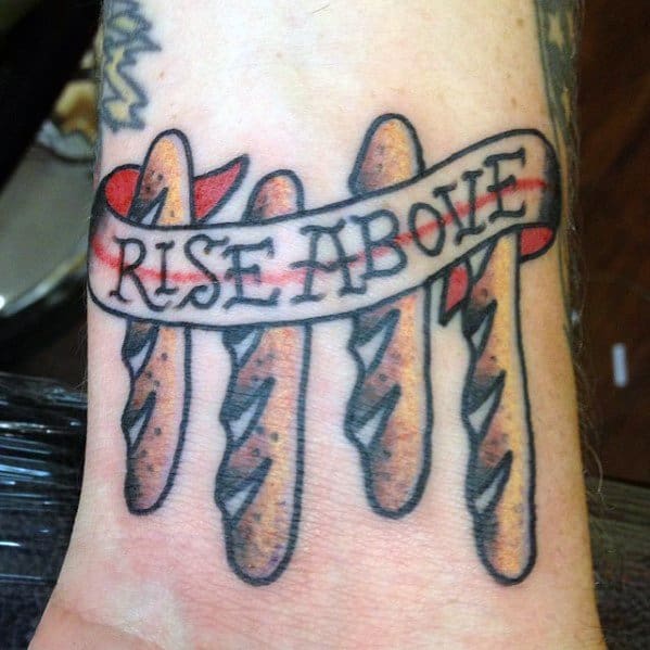 Colorful tattoo of four baguettes with a flowing banner that reads "Rise Above," combining bold lettering and shading for a unique bakery-themed design.