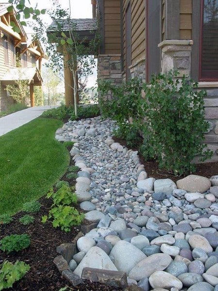 Charming river rock landscaping along the side of a home, with smooth pebbles and greenery creating a neat and natural border.