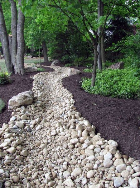 Natural river rock path winding through a lush backyard, bordered by trees and mulch, creating a serene and organic landscape