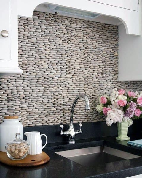 Charming kitchen with a textured river rock backsplash, polished black countertop, and a fresh floral arrangement