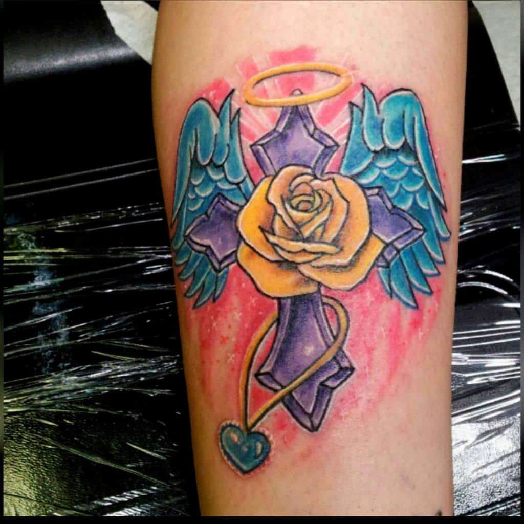 Colorful angel wings tattoo featuring a cross, golden rose, halo, and heart
