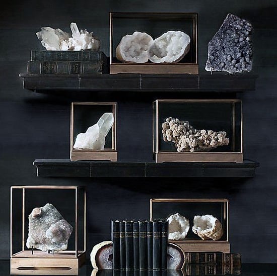 Elegant crystal and geode collection in glass cases on dark shelves with books.