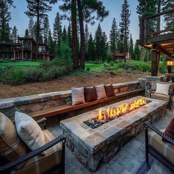 Outdoor seating area with a cozy fire pit, surrounded by trees and rustic houses in the background