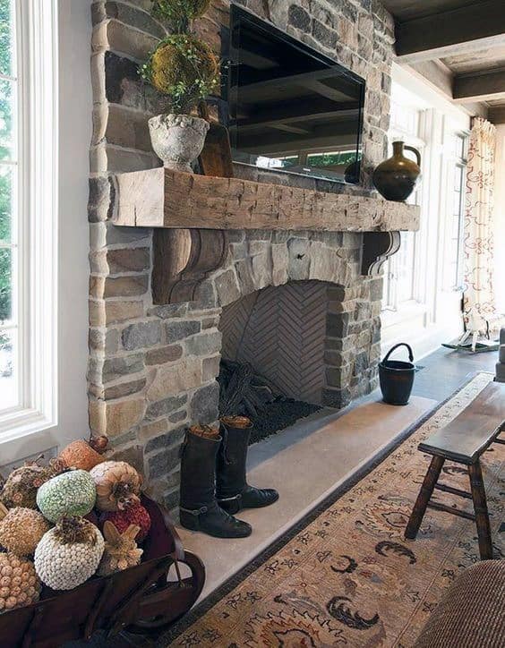 Rustic stone fireplace with wooden mantel, mounted TV, decorative vases, and cozy decor elements.