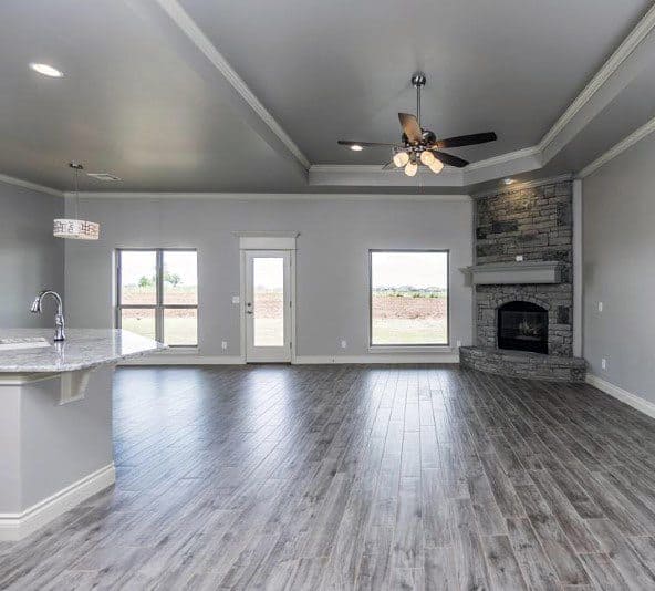 Open living room with gray stone corner fireplace, vaulted ceiling, and wood-look tile flooring.