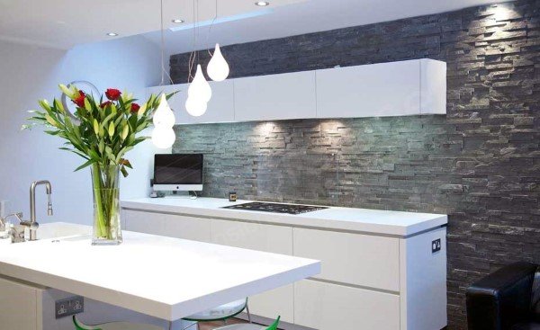 Modern kitchen with textured stone backsplash, white cabinets, and pendant lighting.